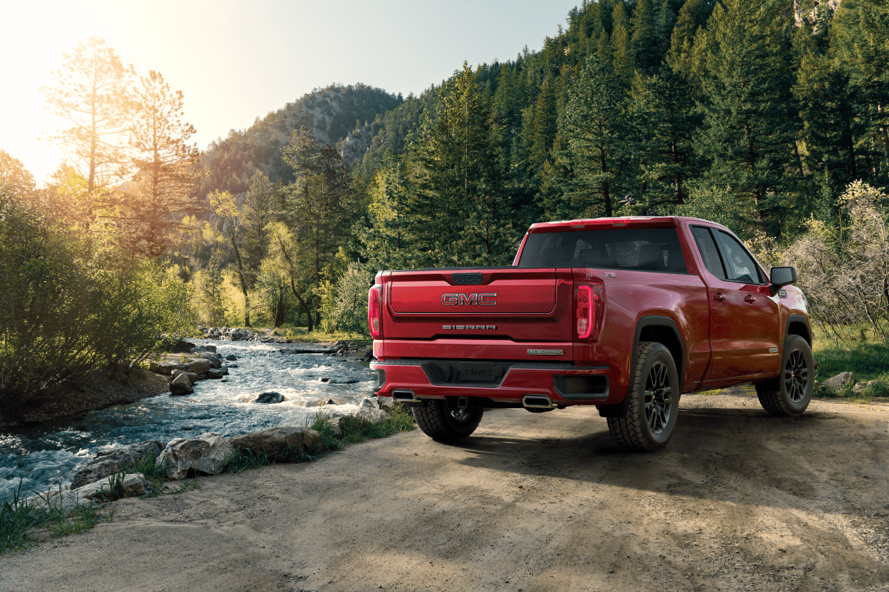 Red GMC Sierra pickup truck parked beside a scenic forest stream.