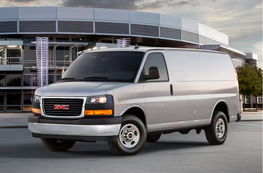 Silver GMC Savana cargo van parked in front of a modern building.