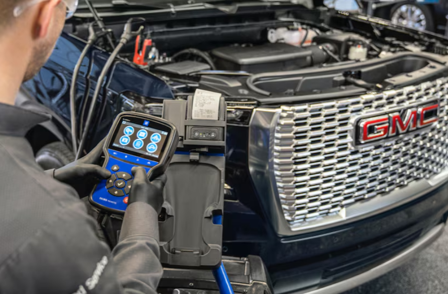 echnician using a diagnostic tool on a GMC vehicle with the hood open in Peruzzi Buick GMC service center.